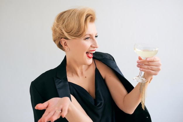 Riendo caucásica madura mujer elegante con estilo en esmoquin con una copa de vino espumoso. fiesta, celebridad