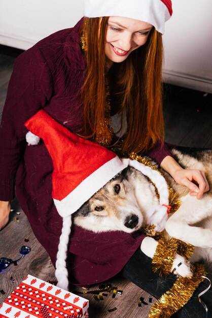 Foto riendo chica pelirroja con una gorra roja sentada en el suelo con su perro, celebra el año nuevo