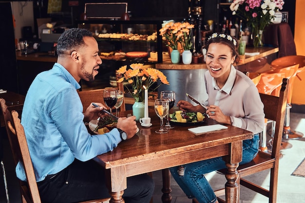 Riendo hermosa pareja afroamericana enamorada pasando un buen rato juntos en su cita, una pareja atractiva disfrutando el uno del otro, comiendo en un restaurante.