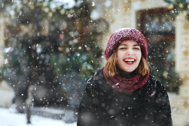 Riendo a joven lleva gorra roja caminando en la ciudad durante las nevadas. Espacio vacio