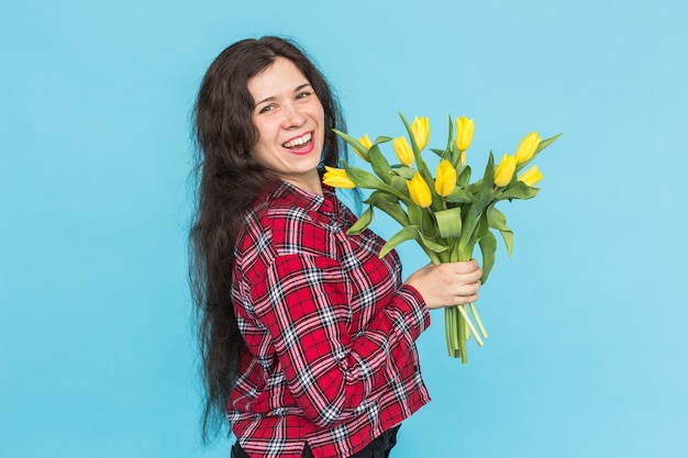 Riendo a joven mujer caucásica con ramo de tulipanes en la pared azul