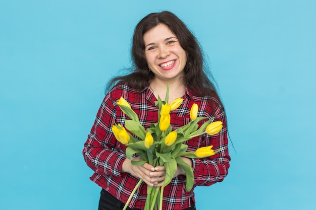 Riendo a joven mujer caucásica con ramo de tulipanes sobre fondo azul.