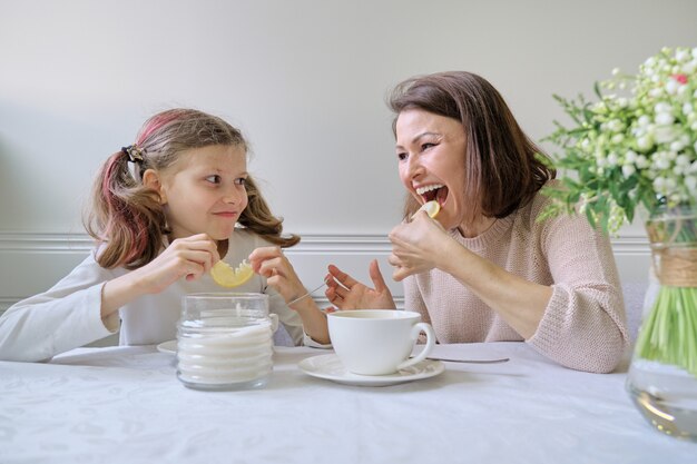 Riendo madre e hija bebiendo de tazas y comiendo limón