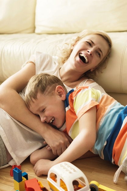 Riendo, madre e hijo jugando en casa durante el fin de semana soleado