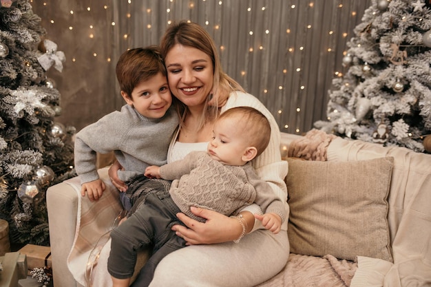 Riendo a mamá e hijos sentados en el sofá cerca del árbol de Navidad en la habitación