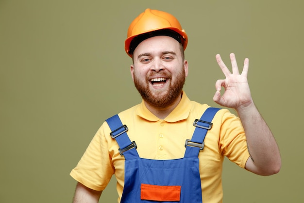 Riendo mostrando bien gesto joven constructor hombre en uniforme aislado sobre fondo verde