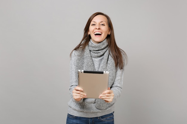 Riendo a mujer joven en suéter, bufanda con tablet pc, haciendo videollamadas aisladas sobre fondo gris. Estilo de vida saludable, consultoría de tratamiento en línea, concepto de estación fría. Simulacros de espacio de copia.