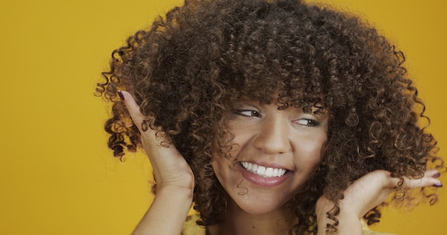 Foto riendo a mujer rizada en suéter tocando su cabello y mirando a la cámara