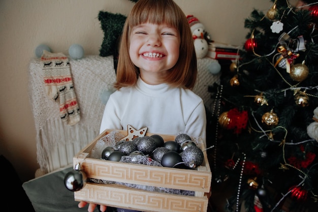 Riendo a niña caucásica con caja de decoración en casa con adornos navideños