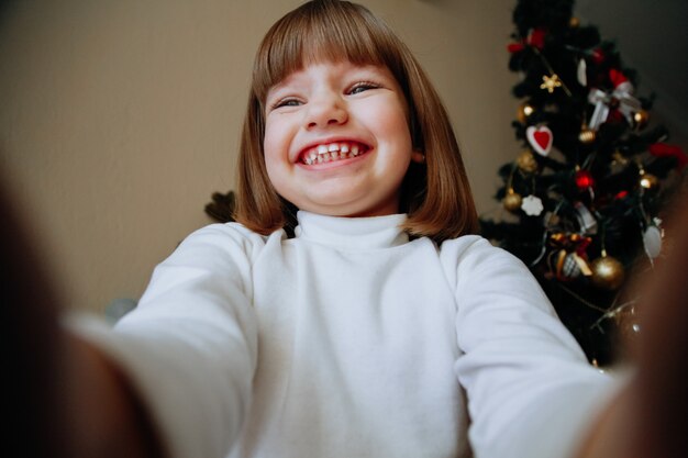 Riendo a niña caucásica tomando selfie en casa con decoraciones. Concepto de niños sonrientes felices.