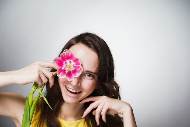 Riendo niña de ojos azules con un vestido amarillo sostiene una flor rosa, celebra el día mundial de la mujer