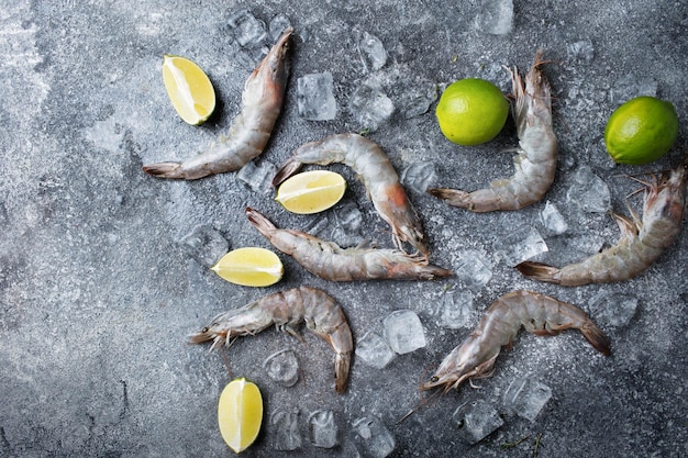 Riesengarnelen und Eis auf grauem Hintergrund Rohe Meeresfrüchte auf einem dunklen Tisch Frische Garnelen mit Limette