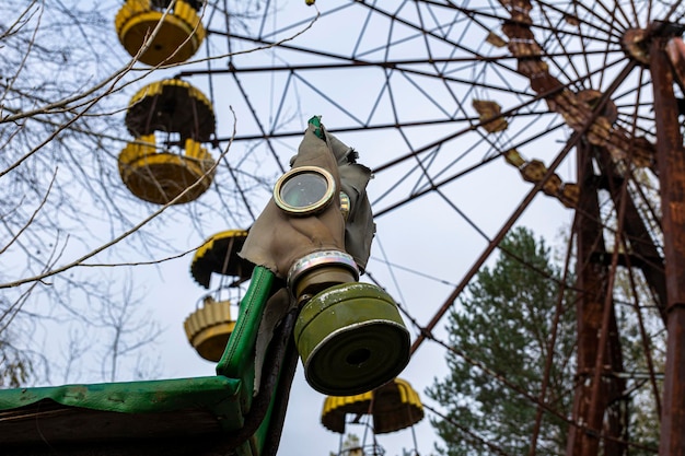 Riesenrad und grüne alte Gasmaske in der Stadt Pripyat. Foto durch rostigen Stacheldraht. 30 km Sperrzone von Tschernobyl. trüber grauer Herbsttag, depressives Wetter und ein verlassener Vergnügungspark