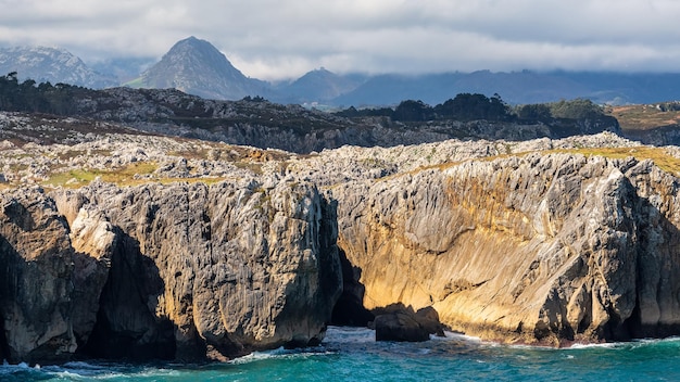 Riesige Klippen vor der Küste Nordspaniens mit den hohen Bergen der Picos de Europa im Hintergrund Asturien