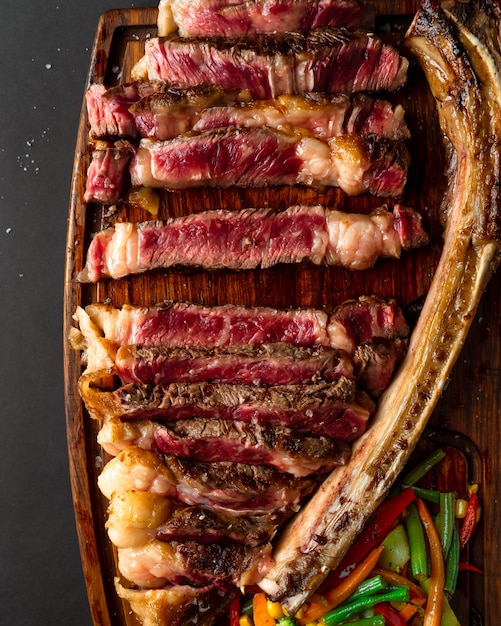 Foto riesiges steak mit einem in stücke geschnittenen knochen, serviert auf holzbrett, detailansicht. von oben geschossen. hochformat