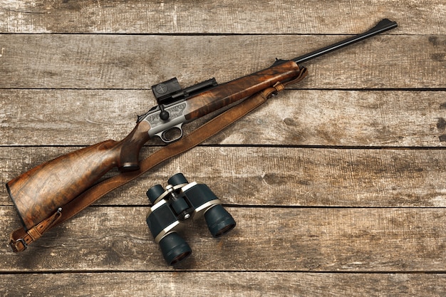 Rifle de caça e binóculos em fundo escuro de madeira