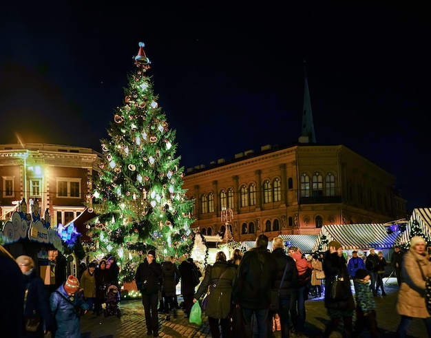 Riga, Letônia - 24 de dezembro de 2015: Pessoas e árvore de Natal no mercado festivo de Natal. A praça Dome no centro da antiga Riga, Letônia. À noite