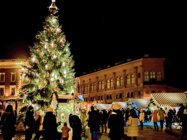 Riga, Letonia - 24 de diciembre de 2015: Gente y árbol de Navidad en el mercado festivo de Navidad en la plaza Dome en el centro de la antigua Riga, Letonia. Por la noche