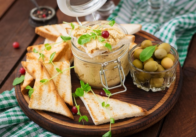 Rillette, Toast, Oliven und Kräuter auf einem Holzbrett. .