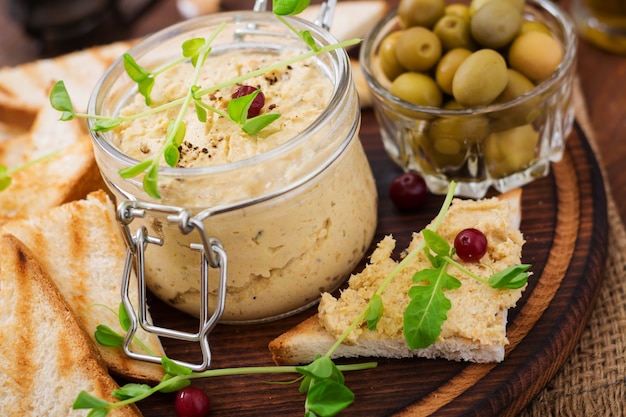 Foto rillette, tostadas, aceitunas y hierbas en una tabla de madera. .