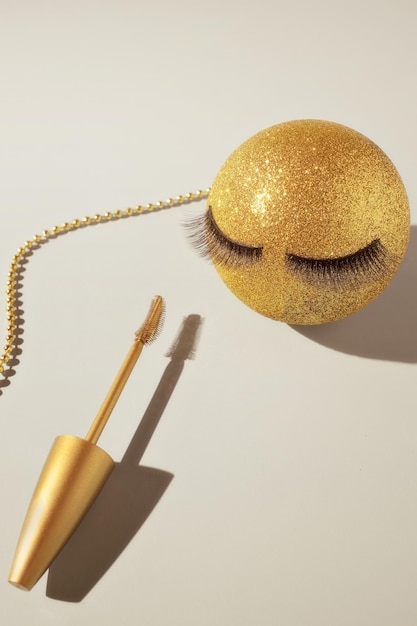 Rimel y una bola dorada de Navidad con pestañas postizas El concepto de maquillaje festivo para mujeres
