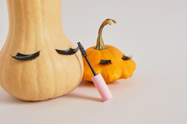 Rímel en empaque rosa simulado en blanco, calabaza y calabaza con pestañas postizas en el espacio de copia de fondo gris, concepto de maquillaje estacional de otoño