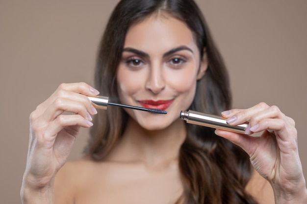 Rímel. Mulher de cabelo comprido sorridente abrindo rímel e segurando as mãos na altura do rosto