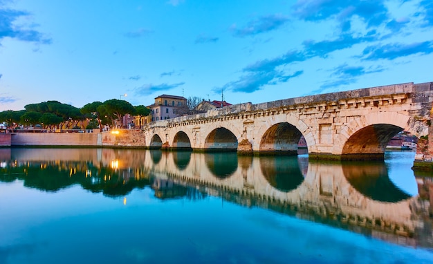 Rimini mit Tiberiusbrücke in der Abenddämmerung, Emilia-Romagna, Italien. Landschaft mit Wasserreflexion. Italienische Architektur