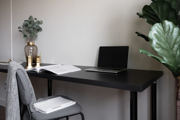 Rincón de trabajo de dormitorio decorado con velas blancas para computadora portátil y planta artificial en florero de vidrio sobre mesa de trabajo de madera con fondo de pared pintada de color beige