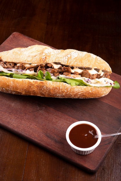 Rinderbrust-Sandwich mit Rucola und Krautsalat auf Baguettebrot auf Holzbrett mit Barbecue-Sauce im Eckporträt