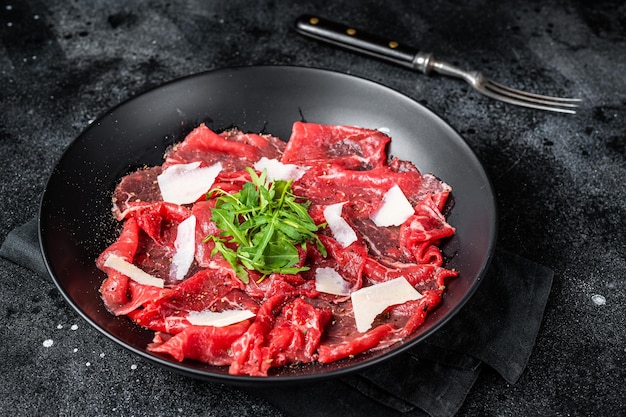 Rindercarpaccio kalte Vorspeise mit Parmesan und Rucola auf einem Teller Schwarzer Hintergrund Ansicht von oben