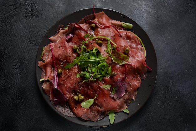 Rindercarpaccio mit Parmesan, Kapern und Rucola. Mit Olivenöl und Sojasauce