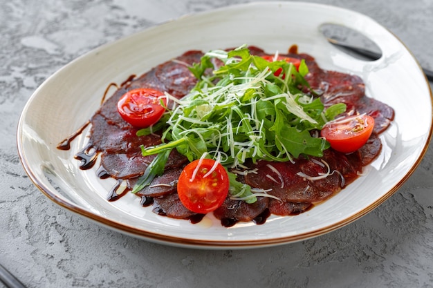 Rindercarpaccio mit Rucola und Parmesan auf grauer Oberfläche