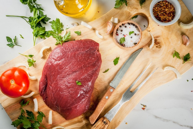 Rinderfiletfilet kochen. Großes ganzes Stück Kalbsfilet auf Schneidebrett mit einer Gabel für Fleisch, Gewürze (Salz, Pfeffer, Petersilie, Knoblauch, Zwiebeln, Tomaten). Kopieren Sie Platz