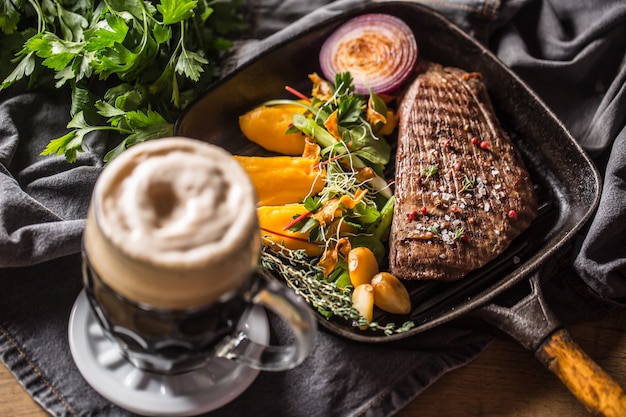 Rinderflanksteak in Grillpfanne mit Batata-Püree-Knoblauch-Kräuter-Dekoration und Fassbier.