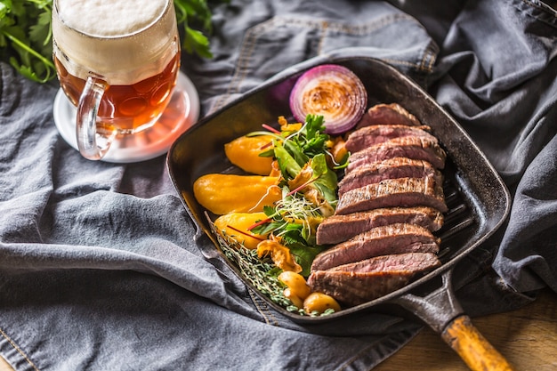 Rinderflanksteak in Grillpfanne mit Batata-Püree-Knoblauch-Kräuter-Dekoration und Fassbier.