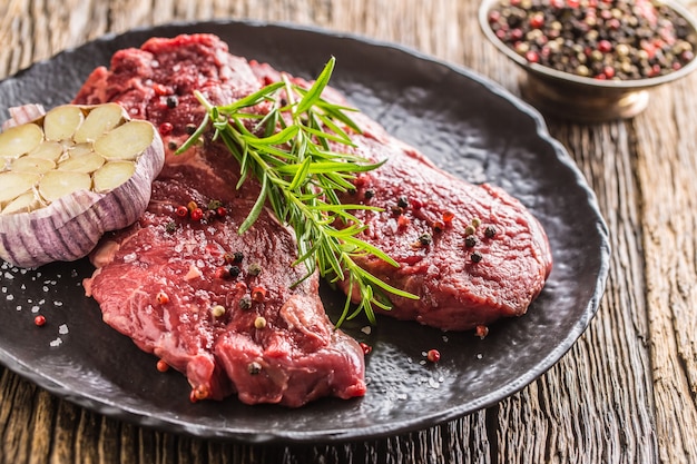 Rinderfleisch Rib-Eye Steak mit Rosmarinsalz und Pfeffer auf schwarzem Teller.