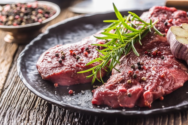Rinderfleisch Rib-Eye Steak mit Rosmarinsalz und Pfeffer auf schwarzem Teller.