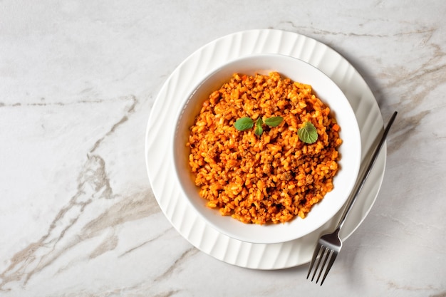 Rinderhack-Risotto Bolognese in einer weißen Schüssel auf einem Marmortisch, italienische Küche, horizontale Ansicht von oben, flach, freier Raum