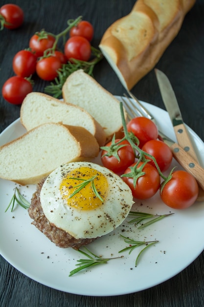 Rindersteak mit Spiegelei in Gewürzen serviert auf einem weißen Teller. Amerikanisches Gericht. Dunkler hölzerner Hintergrund. Seitenansicht. Nahaufnahme.