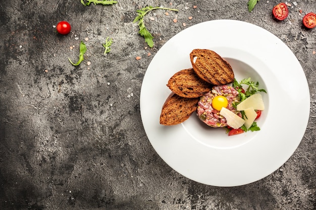 Rindersteak-Tartar mit rohem Wachteleigelb, eingelegter Gurke und Zwiebeln, frischen Kräutern, Brot. Französische Küche, Banner, Menü, Rezeptplatz für Text, Draufsicht.