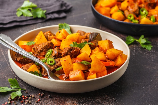 Rindfleisch gedünstet mit Kartoffeln in Tomatensauce, dunkler Hintergrund.