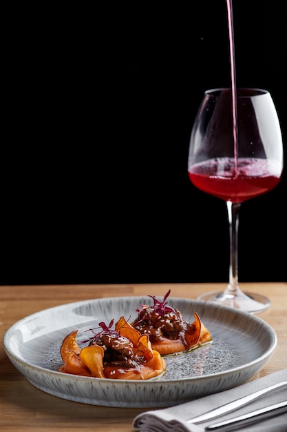 Rindfleisch mit Soße und Süßkartoffel auf einem Tisch im Restaurant mit einem Glas Wein, Abendessen im Restaurant mit dunklem Hintergrund