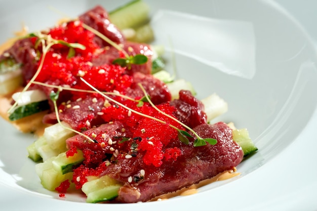 Rindfleisch-Tataki mit Gurke, Tobiko-Kaviar und Sauce in einem weißen Teller. Farbige Hintergründe. Hartes Licht. selektiver Fokus