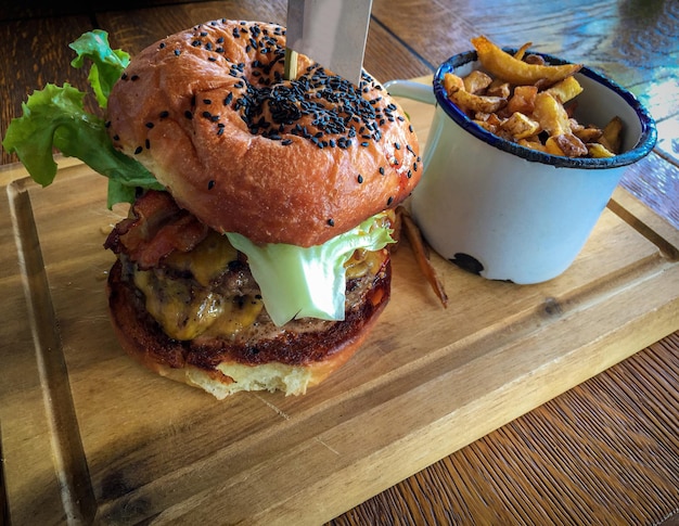 Rindfleischburger mit Pommes Frites auf Holztischhintergrund. Köstliches saftiges leckeres Hamburger-Sandwich mit Brot, Fleisch, Käse, Zwiebeln, Sauce und frischem Salat. Restaurant-Fastfood. Mahlzeit mit Snack