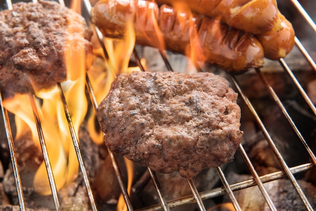 Rindfleischburger und -würste, die über Flammen auf Grill kochen