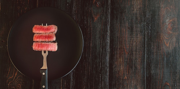 Rindfleischsteak auf einer Gabel auf einer dunklen Holzoberfläche