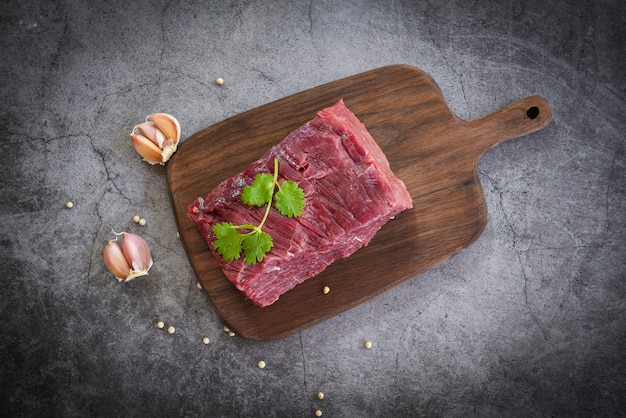 Rindfleischsteak des rohen Fleisches mit Gewürzknoblauch auf hölzernem Schneidebrett und schwarzem Hintergrund