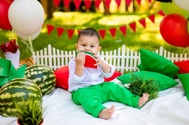 Rindo bebê 1-2 anos de idade comendo melancia ao ar livre. Conceito de festa de verão