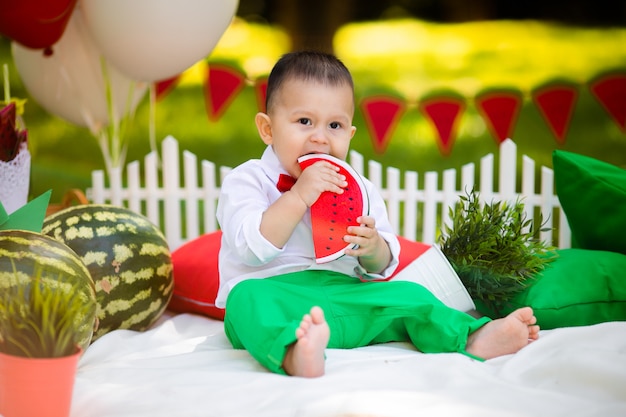 Rindo bebê 1-2 anos de idade comendo melancia ao ar livre. Conceito de festa de verão